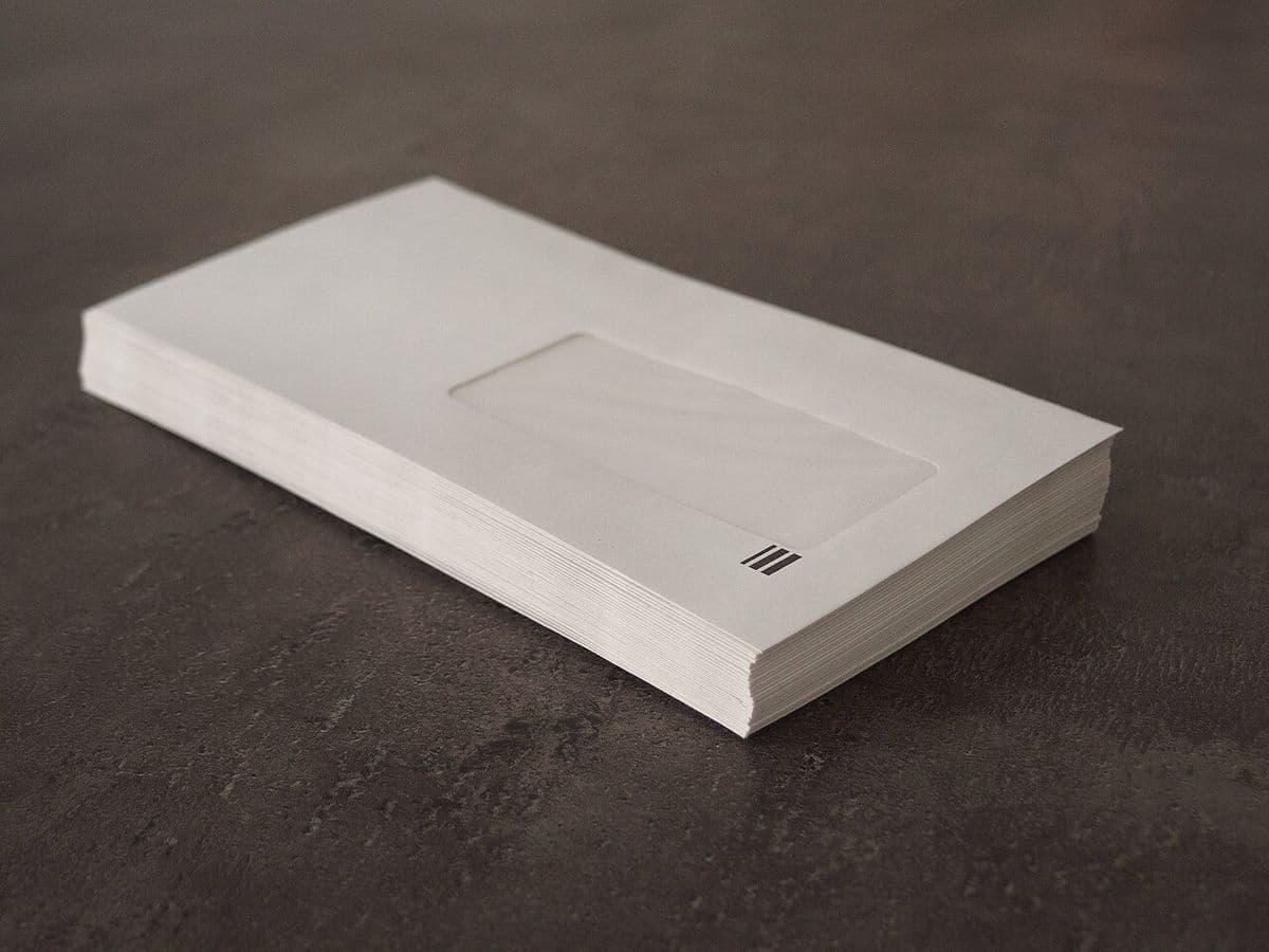 A stack of white window envelopes on a dark table