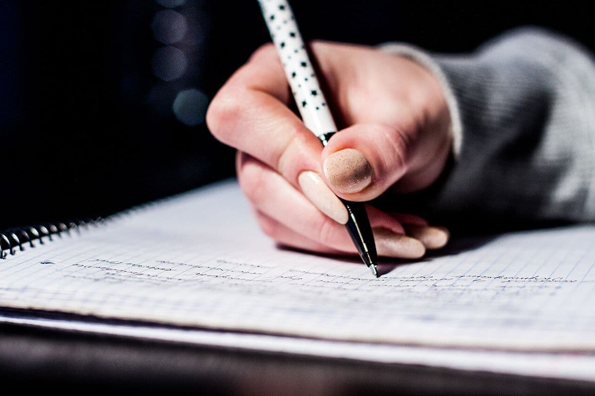 A hand writing notes with a pen on squared paper